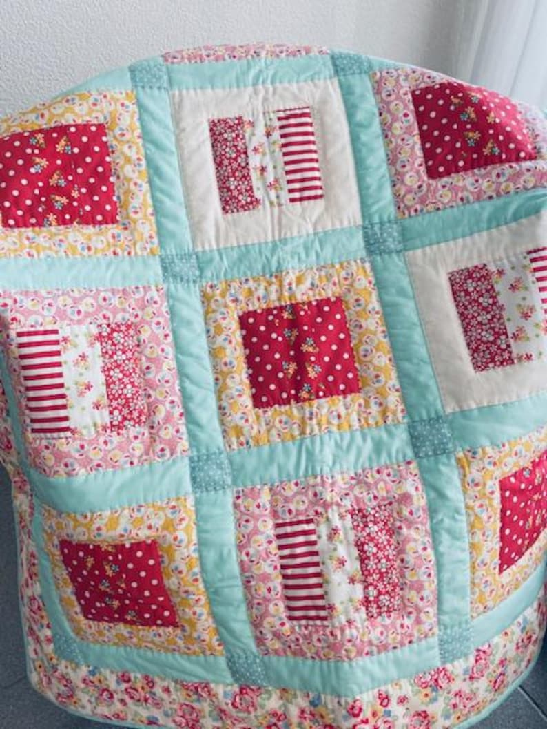 Könnte beinhalten: Eine Patchwork-Decke mit hellblauem Hintergrund und Quadraten in verschiedenen floralen und geometrischen Mustern in Rot, Rosa und Gelb.