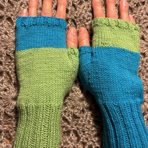May include: A pair of fingerless gloves with a green and blue color block design. The gloves are knitted and have a ribbed cuff.