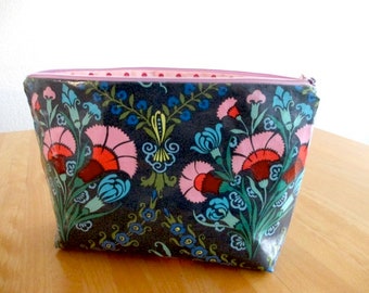Könnte beinhalten: Eine graue Reißverschlusstasche mit einem Blumendruck mit rosa, roten, blauen und grünen Blumen auf einem dunkelgrauen Hintergrund.