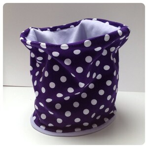 Könnte beinhalten: Lilafarbener Halsschmeichler mit weißen Punkten. Der Halsschmeichler ist aus weichem, dehnbarem Stoff gefertigt und mit einem helllila Stoff gefüttert.