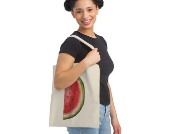 May include: A woman is holding a beige tote bag with a watermelon graphic. The watermelon is red with black seeds and a green rind.