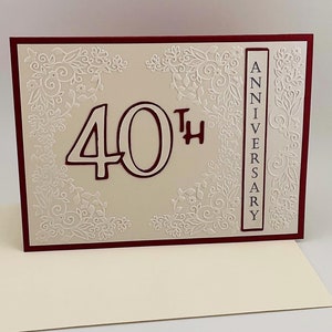May include: A white card with a red border and a white embossed design. The card says "40th Anniversary" in a vertical column on the right side and "40th" in large numbers on the left side.