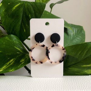 May include: A pair of black and white patterned hoop earrings with black round accents. The earrings are displayed on a white card.