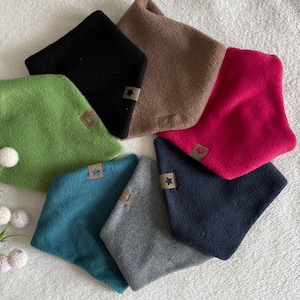 Könnte beinhalten: Sieben Fleece-Halswärmer in verschiedenen Farben, darunter Grün, Schwarz, Braun, Pink, Türkis, Grau und Dunkelblau. Jeder Halswärmer hat einen sternförmigen Ausschnitt mit einem braunen Lederfleck.