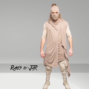 Puede incluir: Una persona que lleva una capucha beige con una bufanda larga, pantalones beige y botas beige. La persona lleva una máscara facial beige. El texto "RAGS BY JAK" es visible en la parte inferior central de la imagen.