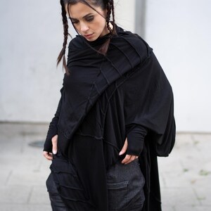 K&ouml;nnte beinhalten: Schwarzes, drapiertes Oberteil mit langen &Auml;rmeln und einem einzigartigen Nahtdesign. Das Oberteil wird mit dunkelgrauen Jeanshosen kombiniert. Das Outfit hat eine moderne, avantgardistische &Auml;sthetik. Das Model tr&auml;gt das Outfit.