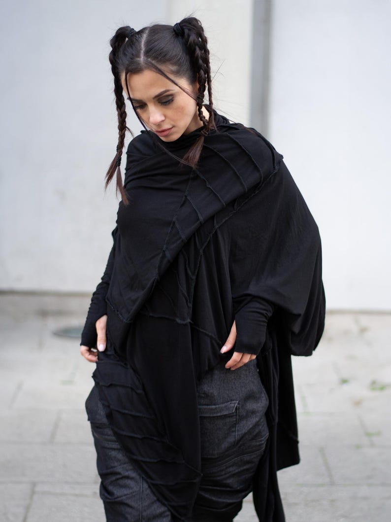 K&ouml;nnte beinhalten: Schwarzes, drapiertes Oberteil mit langen &Auml;rmeln und einem einzigartigen Nahtdesign. Das Oberteil wird mit dunkelgrauen Jeanshosen kombiniert. Das Outfit hat eine moderne, avantgardistische &Auml;sthetik. Das Model tr&auml;gt das Outfit.