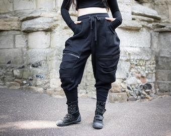 May include: Black joggers featuring a high-waisted design with a drawstring closure, side pockets, and two large zippered cargo pockets on the thighs. The pants have a relaxed fit through the hips and thighs, tapering down to fitted ribbed cuffs.