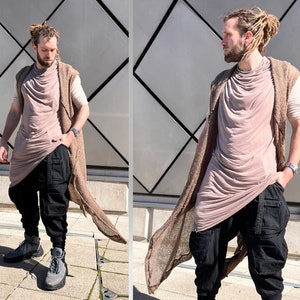 May include: A person wearing a long, brown cardigan over a light brown, draped top and black pants. The person is standing in front of a silver, diamond-patterned wall.