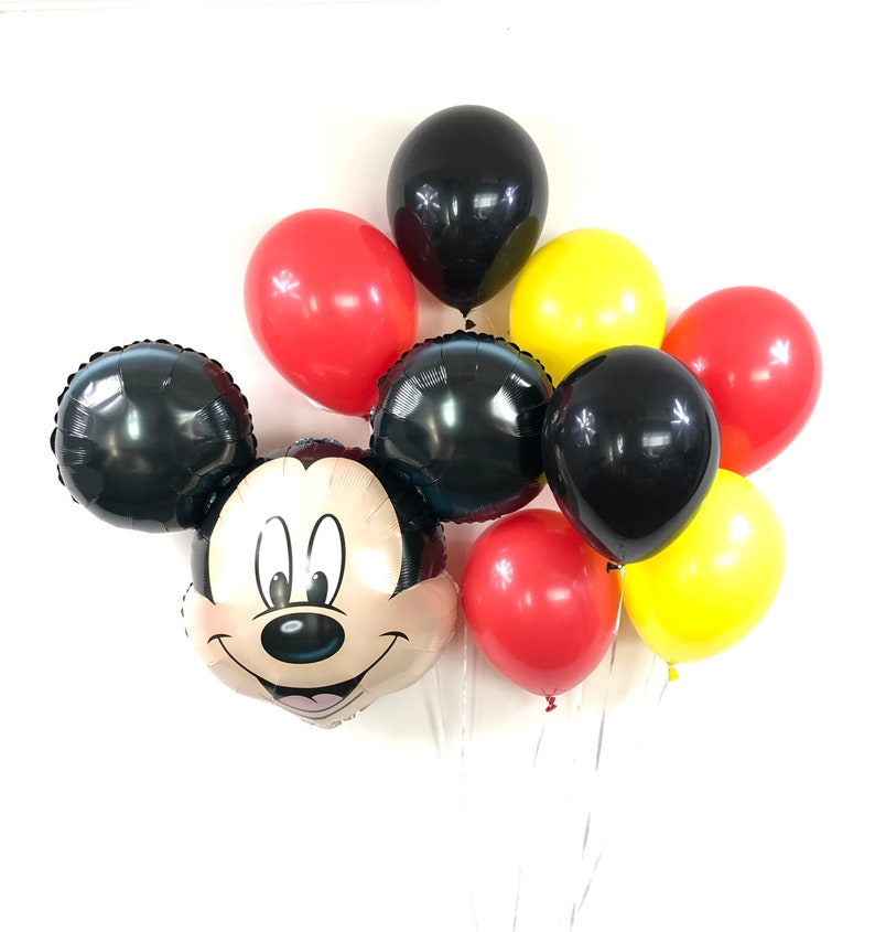 May include: A Mickey Mouse balloon bouquet with black, red and yellow balloons. The Mickey Mouse balloon is a foil balloon with a smiling face.