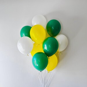 Puede incluir: Un racimo de once globos de l&aacute;tex en colores s&oacute;lidos blanco, amarillo brillante y verde bosque oscuro. Los globos son redondos, est&aacute;n inflados y atados con cintas de pl&aacute;stico transparente delgadas en la base, creando un arreglo multicolor vibrante.