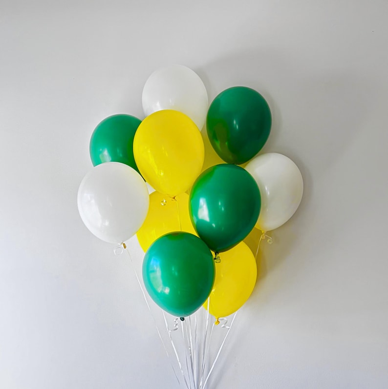 Puede incluir: Un racimo de once globos de l&aacute;tex en colores s&oacute;lidos blanco, amarillo brillante y verde bosque oscuro. Los globos son redondos, est&aacute;n inflados y atados con cintas de pl&aacute;stico transparente delgadas en la base, creando un arreglo multicolor vibrante.