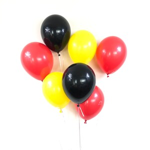 May include: A group of six balloons in red, yellow and black colours. The balloons are tied together and are floating in the air.