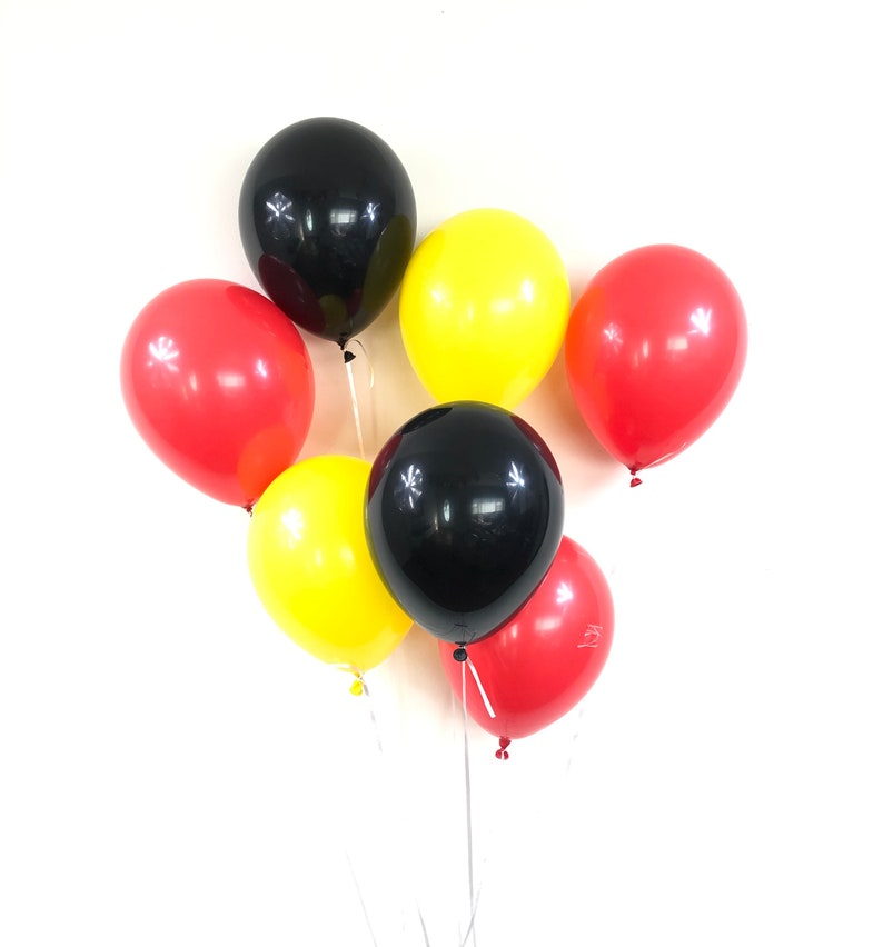 May include: A group of six balloons in red, yellow and black colours. The balloons are tied together and are floating in the air.
