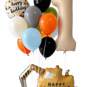 May include: A balloon bouquet featuring a large beige number one foil balloon, a yellow excavator-shaped foil balloon with the text "HAPPY BIRTHDAY", and a round balloon with construction vehicles and "happy birthday" text, plus assorted latex balloons.