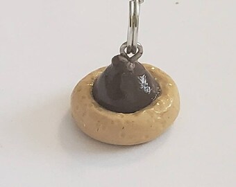May include: A chocolate-filled cookie keychain with a brown chocolate center and a light brown cookie base. The keychain has a silver metal ring.