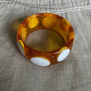 May include: A yellow bangle bracelet with white polka dots and a glittery finish.