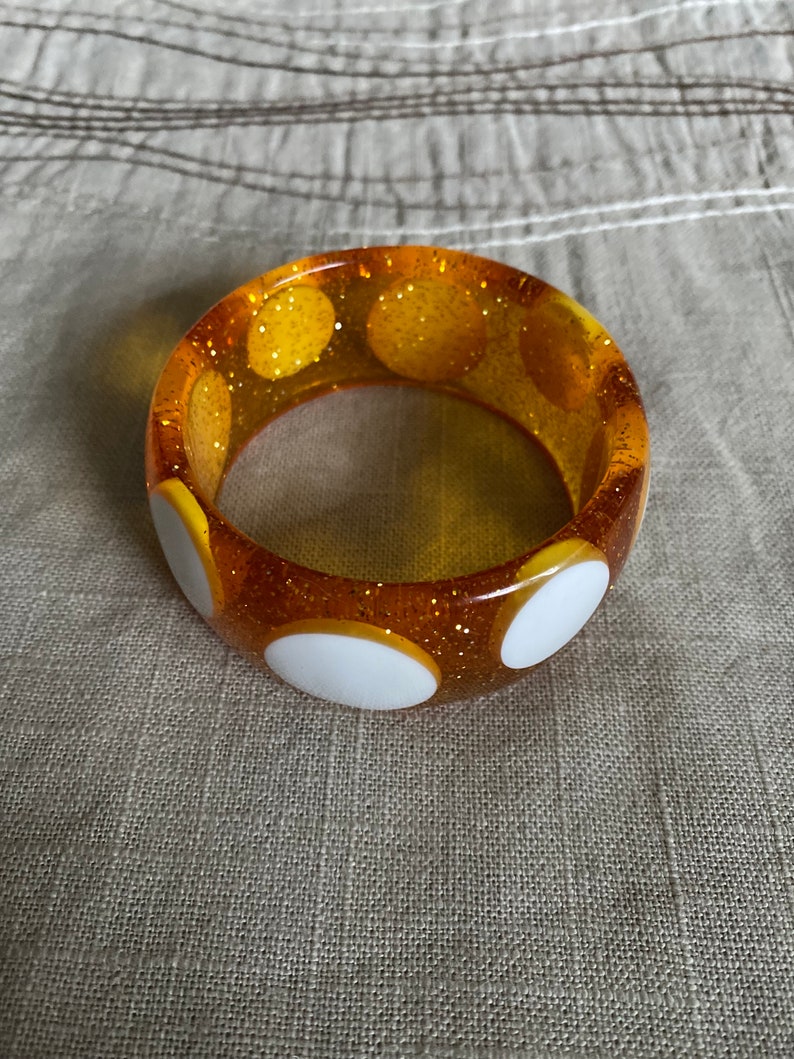 May include: A yellow bangle bracelet with white polka dots and a glittery finish.