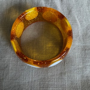 May include: A white and yellow bangle bracelet with gold glitter embedded in the yellow sections.
