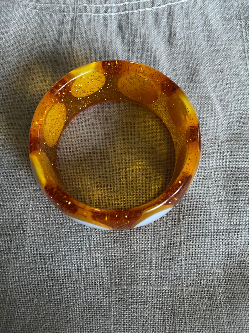 May include: A white and yellow bangle bracelet with gold glitter embedded in the yellow sections.