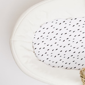 May include: White oval-shaped bassinet with a white and black raindrop patterned sheet. The sheet is labeled "Raindrops Sheet".
