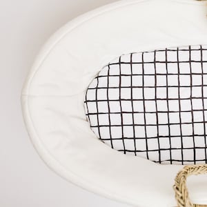 May include: White oval-shaped bassinet with a black and white grid patterned sheet. The sheet is labeled "Modern Grid Sheet".