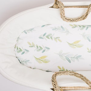 May include: White wicker bassinet with a white and green floral patterned liner. The bassinet has a woven rope handle.