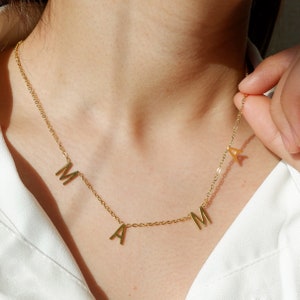 Puede incluir: Un collar de cadena dorada con las letras "MAMA" colgando.