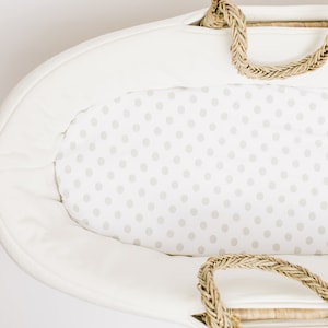 May include: White oval-shaped baby bassinet with a white and gray polka dot fitted sheet. The bassinet has a woven rope handle.