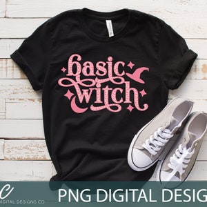 Può includere: Una maglietta nera con una grafica rosa che dice "basic witch" con un cappello da strega e stelle. La grafica ha un motivo leopardato rosa.