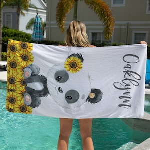 May include: White beach towel with a panda bear and sunflowers printed on it. The towel has the name "Oaklynn" written on it.