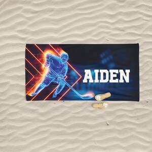 K&ouml;nnte beinhalten: Ein blaues und oranges Strandtuch mit einer Grafik eines Hockeyspielers und dem Namen "AIDEN" darauf.