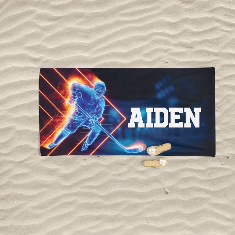K&ouml;nnte beinhalten: Ein blaues und oranges Strandtuch mit einer Grafik eines Hockeyspielers und dem Namen "AIDEN" darauf.