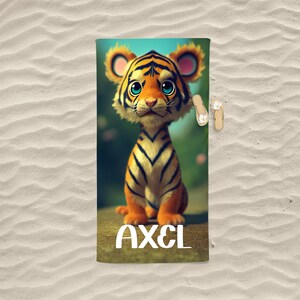 Op de afbeelding: Een strandhanddoek met een cartoon-tijgerillustratie en de naam "AXEL" in witte letters.