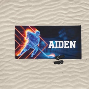 K&ouml;nnte beinhalten: Ein blaues und oranges Strandtuch mit einem Hockey-Spieler-Motiv und dem Namen "AIDEN" darauf.