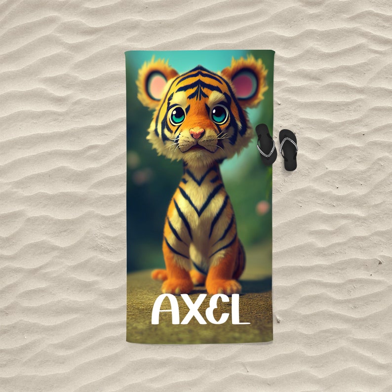 Op de afbeelding: Een strandhanddoek met een cartoon-tijgerillustratie en de naam "AXEL" erop gedrukt. De tijger is oranje en zwart met blauwe ogen en zit op een groene achtergrond.
