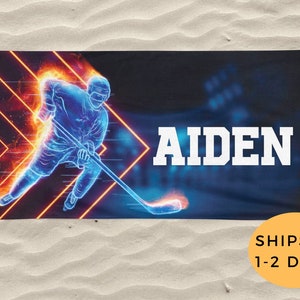 K&ouml;nnte beinhalten: Ein blaues und oranges Strandtuch mit einer Grafik eines Hockeyspielers und dem Namen "AIDEN" in wei&szlig;er Schrift.