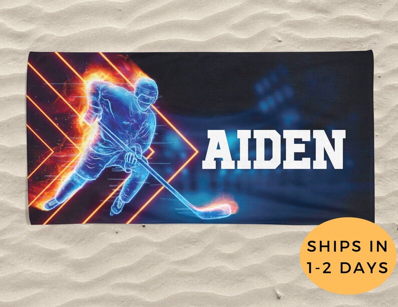 K&ouml;nnte beinhalten: Ein blaues und oranges Strandtuch mit einer Grafik eines Hockeyspielers und dem Namen "AIDEN" in wei&szlig;er Schrift.
