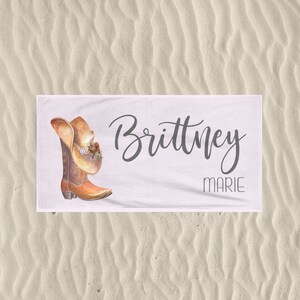May include: White beach towel with a brown cowboy boot and hat design. The text "Brittney Marie" is printed on the towel.