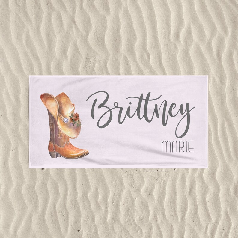 May include: White beach towel with a brown cowboy boot and hat design. The text "Brittney Marie" is printed on the towel.