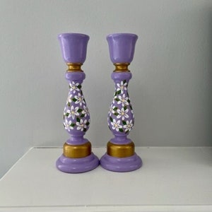 May include: A pair of purple candle holders with white floral designs and gold accents. The candle holders are made of wood and have a classic style.