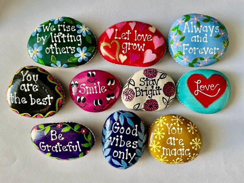 Pode incluir: Uma cole&ccedil;&atilde;o de pedras decorativas pintadas &agrave; m&atilde;o com mensagens inspiradoras. Cada pedra apresenta designs &uacute;nicos, incluindo padr&otilde;es florais, cora&ccedil;&otilde;es e frases inspiradoras como "Smile" e "Good Vibes Only."