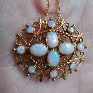 May include: A gold-toned pendant necklace featuring an ornate filigree design. The pendant is adorned with oval and round opals, showcasing iridescent colors. The necklace is suspended from a delicate gold chain.