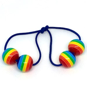 Könnte beinhalten: Ein blaues Haargummi mit drei regenbogenfarbenen Kugeln daran.