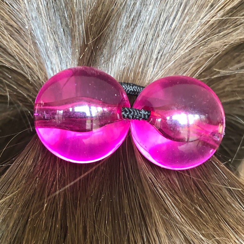May include: A pair of pink hair ties made of clear plastic with a shiny finish.
