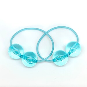 May include: Two light blue hair ties with clear plastic balls on the ends.