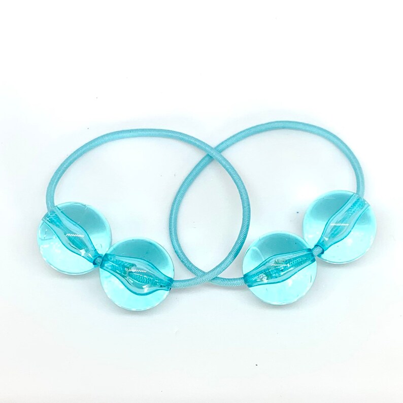May include: Two light blue hair ties with clear plastic balls on the ends.