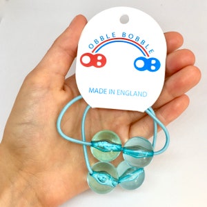 May include: A set of three light blue glass bobbles on a blue elastic hair tie. The hair tie is packaged with a white card that reads "OBBLE BOBBLE" with a rainbow arch and "MADE IN ENGLAND".