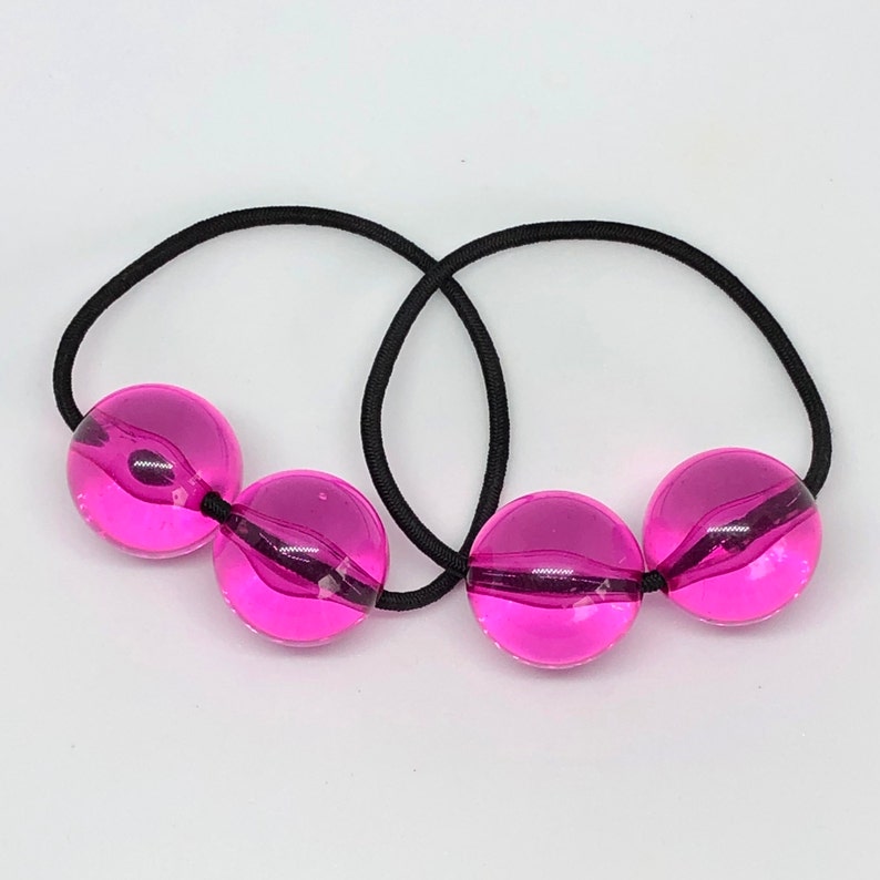 May include: Two black hair ties with three pink, round, translucent beads attached.