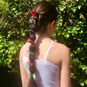 May include: A braided ponytail with colorful plastic hair clips. The clips are in various colors, including red, blue, green, and pink.